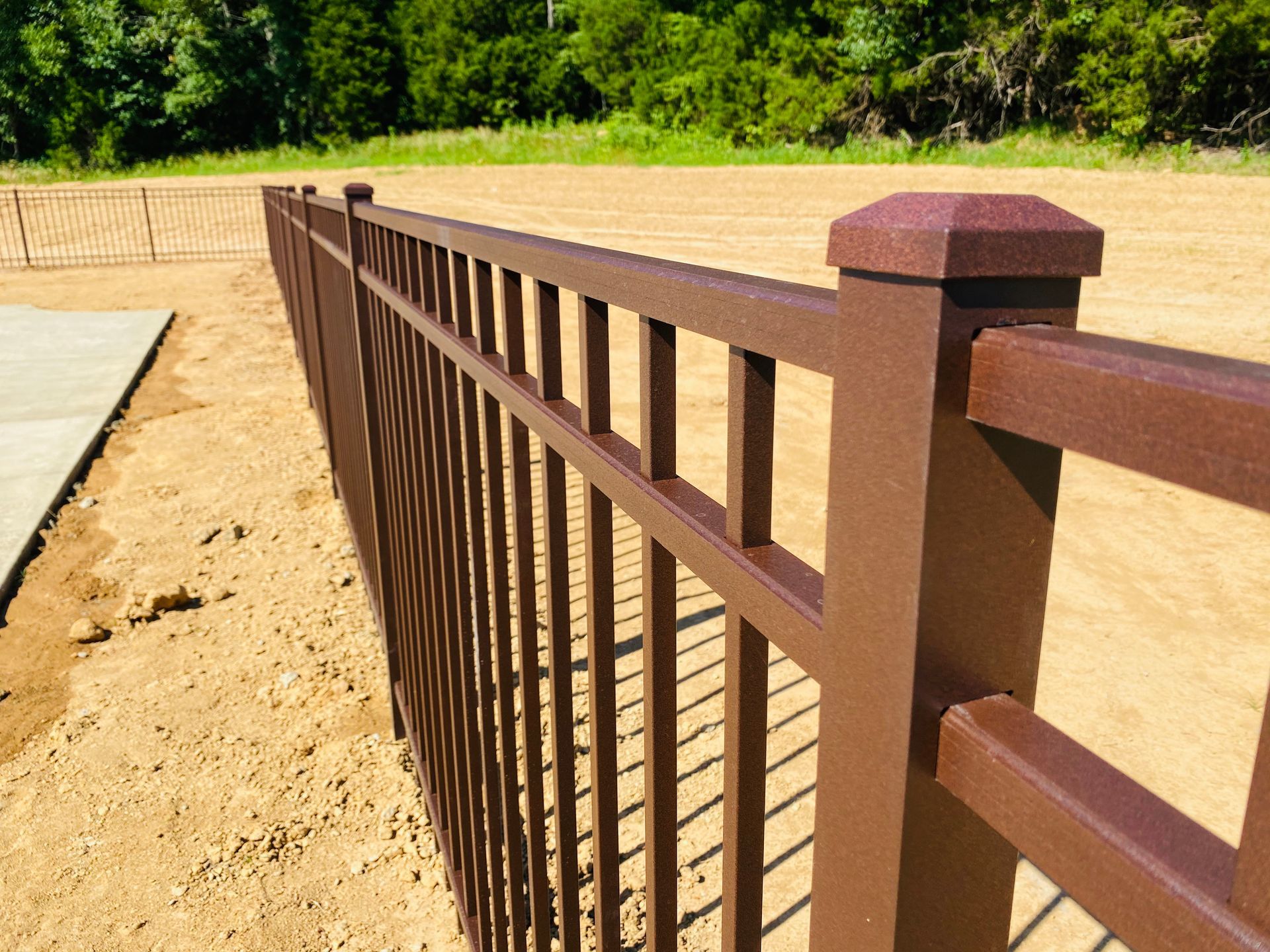 A brown metal fence is surrounded by dirt and trees.