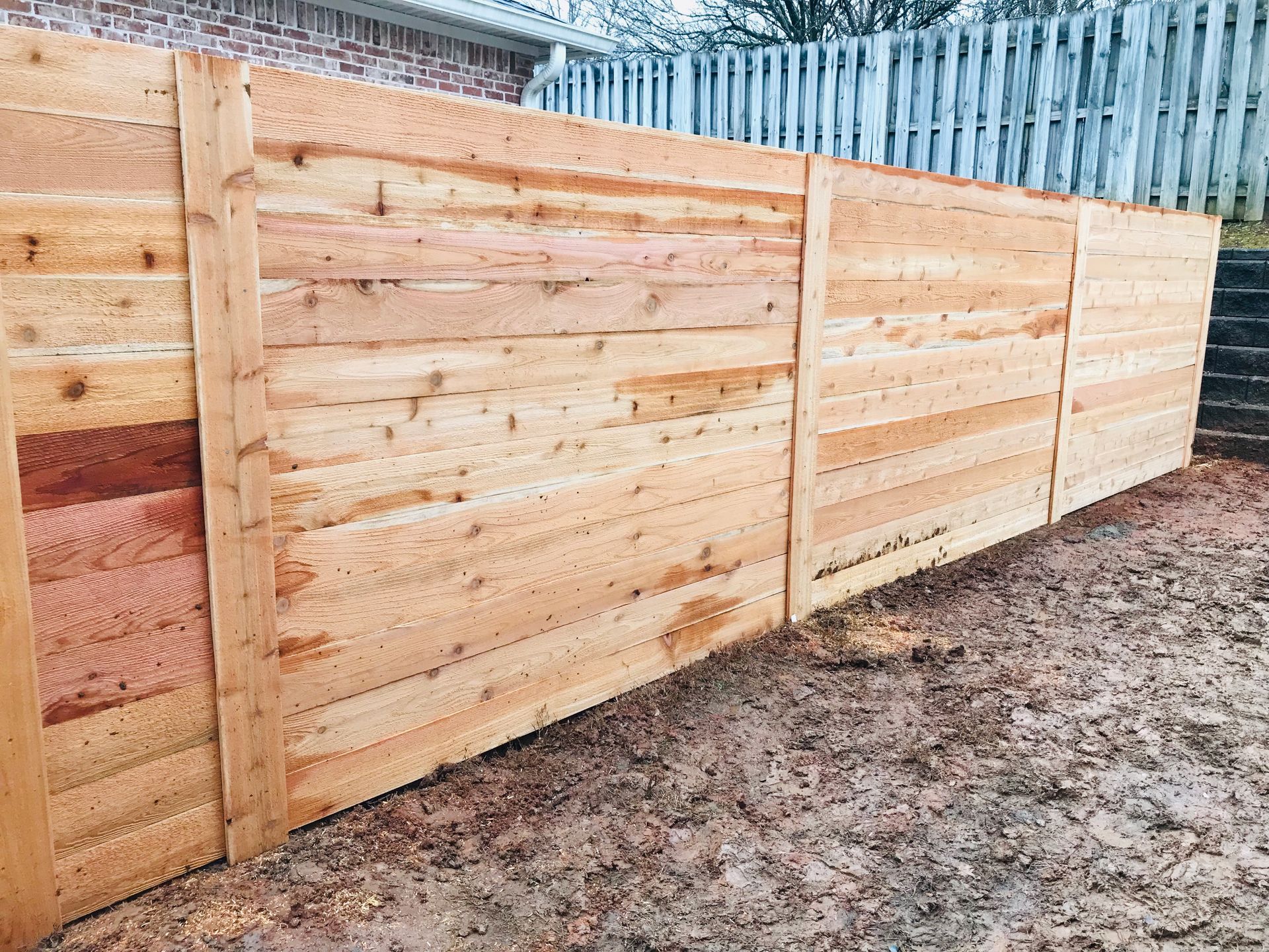 A wooden fence is sitting in the dirt in front of a house.