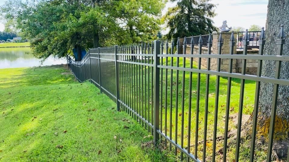 A metal fence surrounds a lush green field next to a lake.