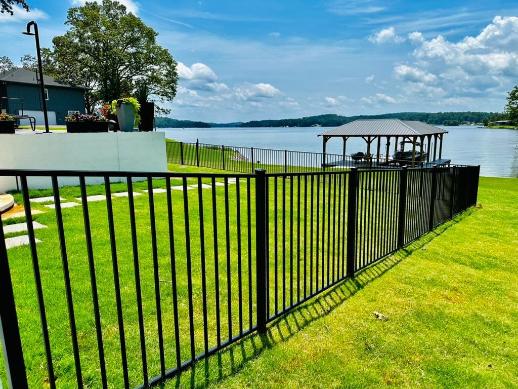 A black fence surrounds a lush green field with a gazebo in the background.