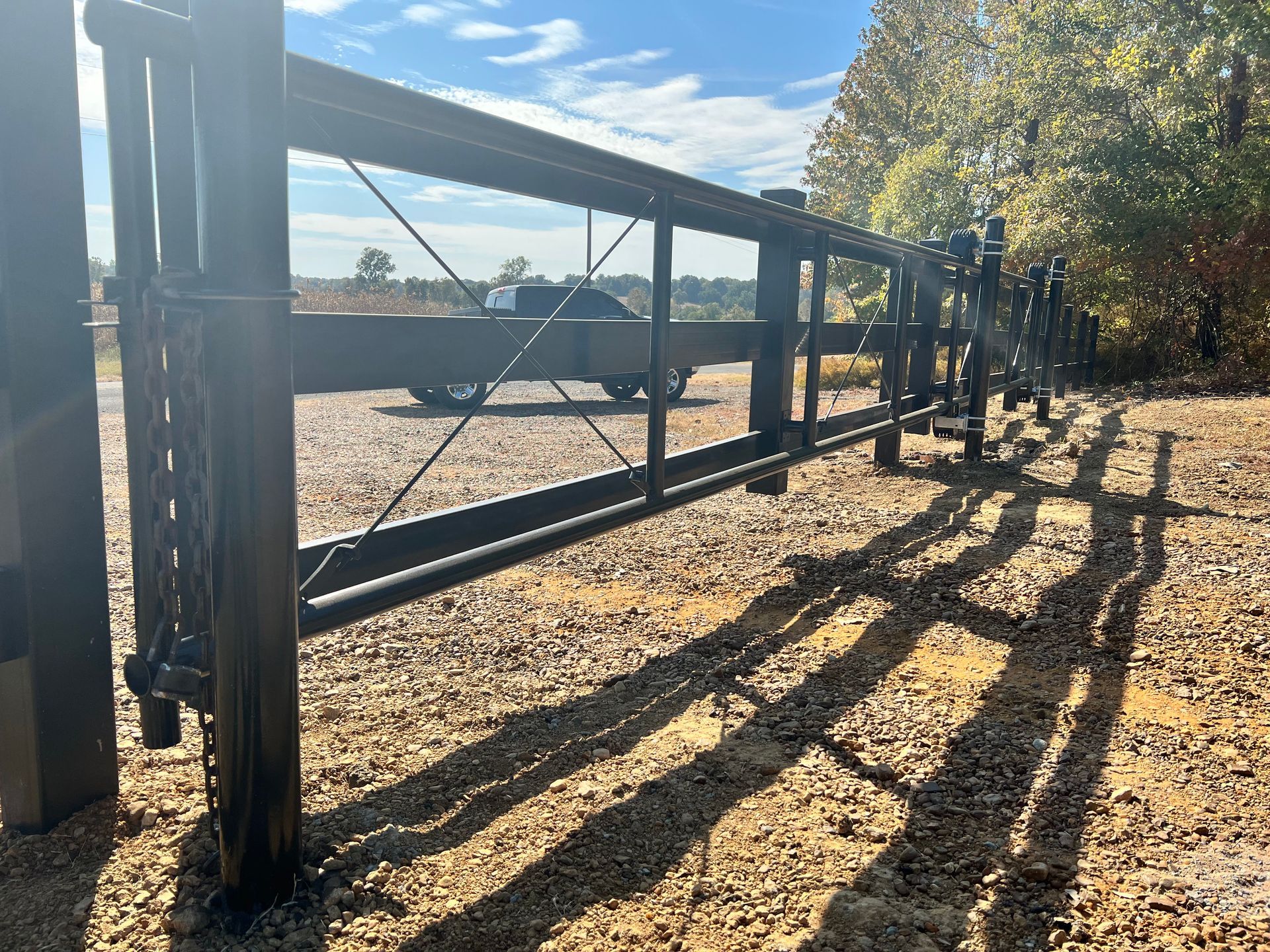 A truck is parked behind a metal gate on a gravel road.