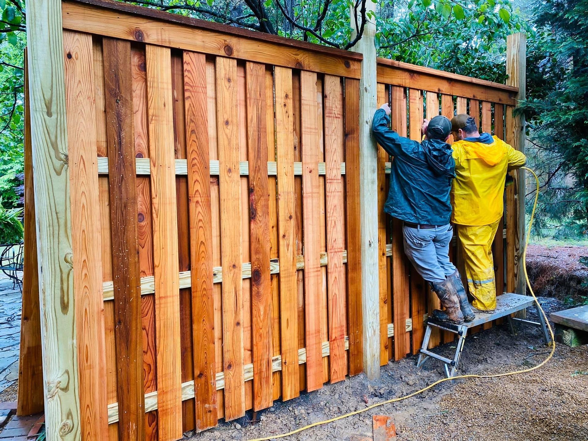 Two men are working on a wooden fence.