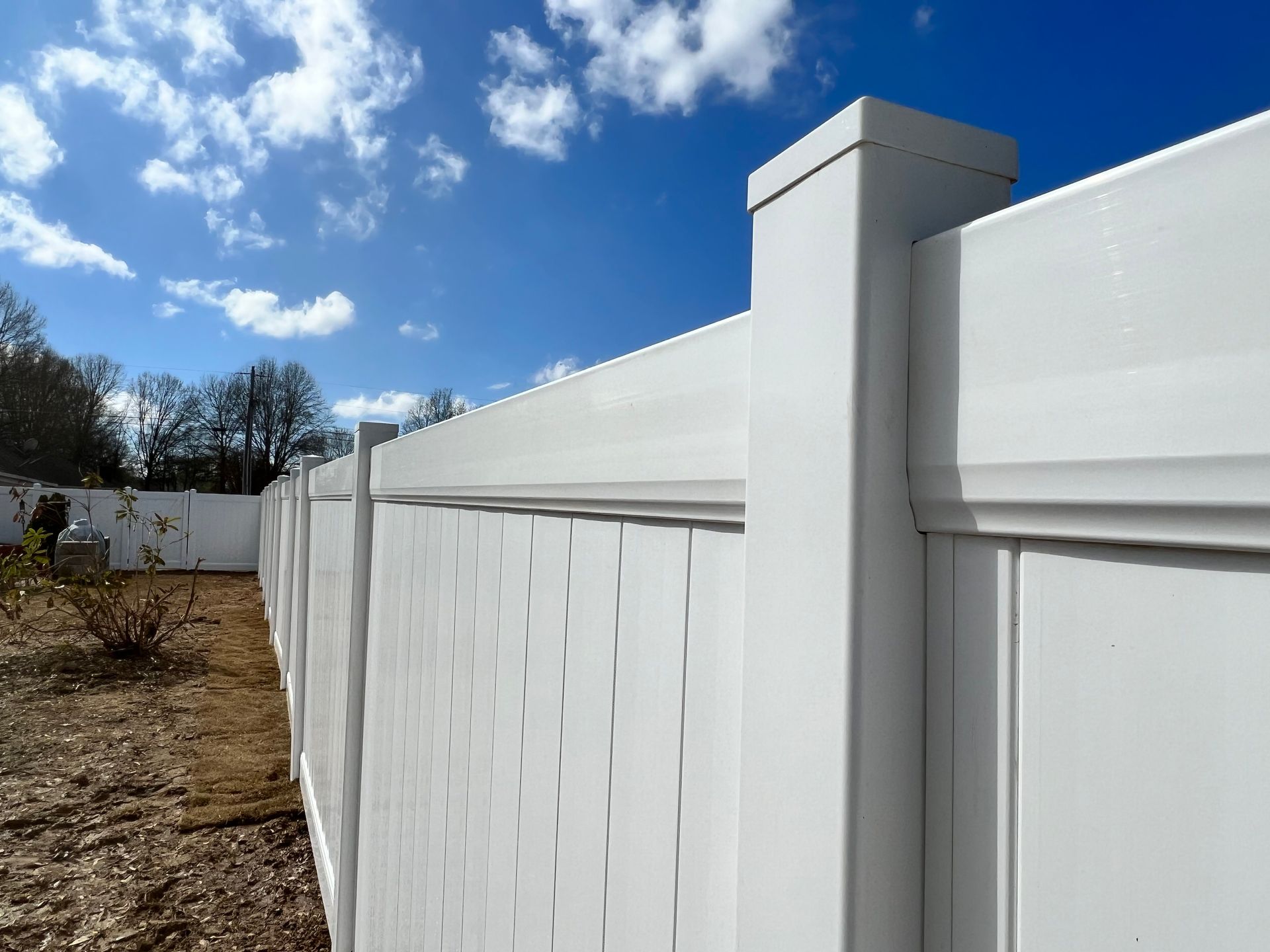 A white vinyl fence with a blue sky in the background.