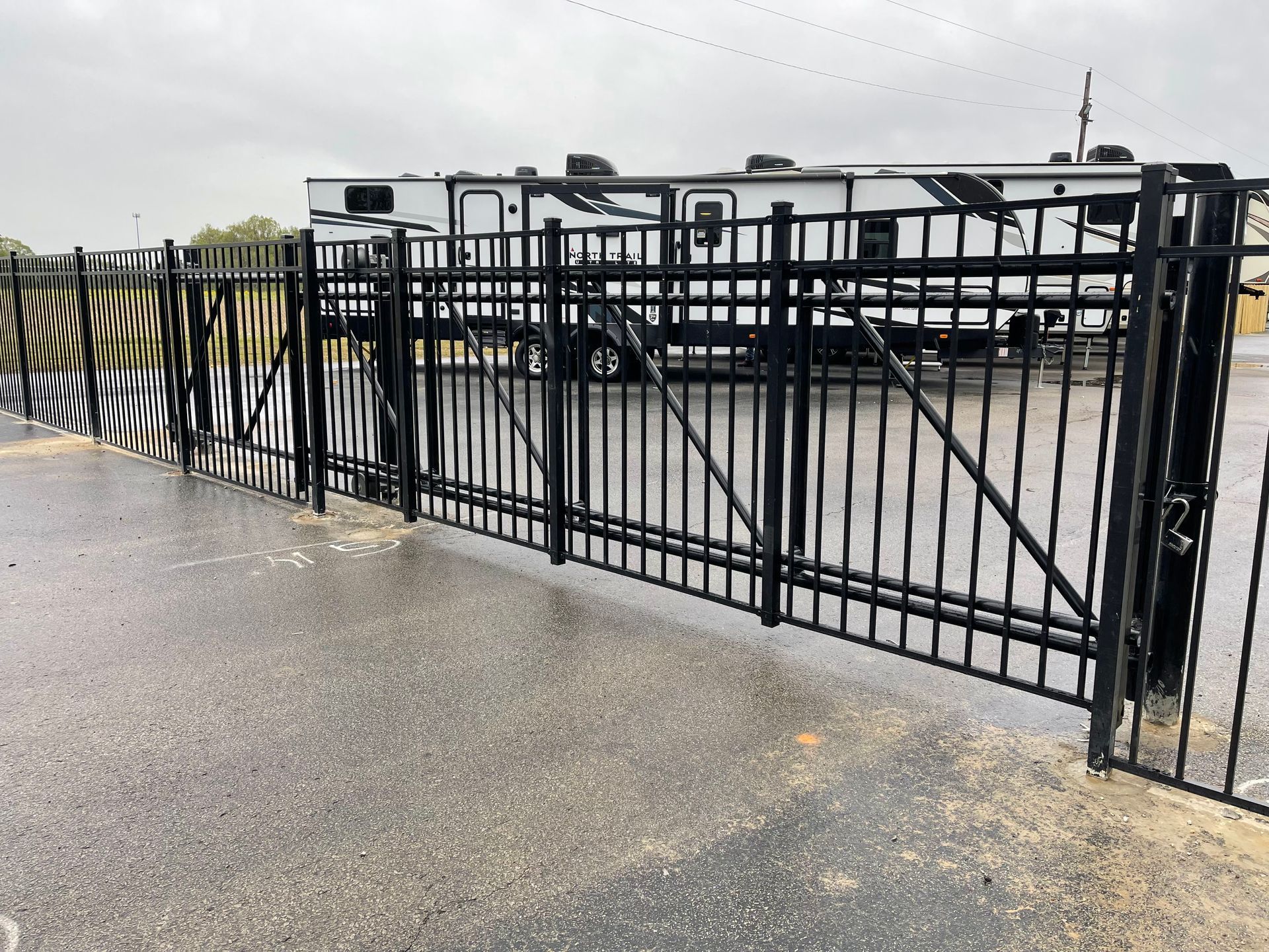 A black wrought iron gate is open to a parking lot.