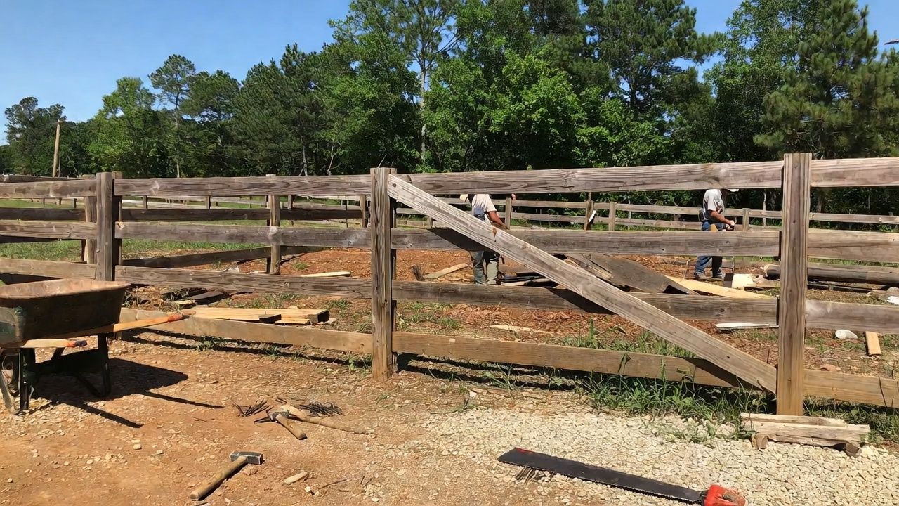 People constructing a wooden fence in a sunny outdoor setting.