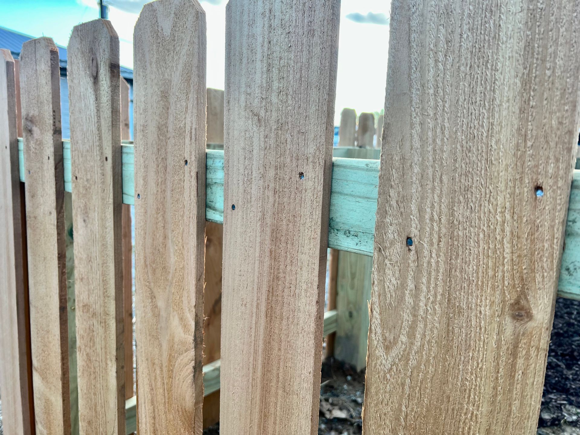 A close up of a wooden picket fence with a blue railing.