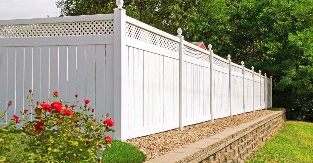 White vinyl fence with lattice top, red roses, and retaining wall.