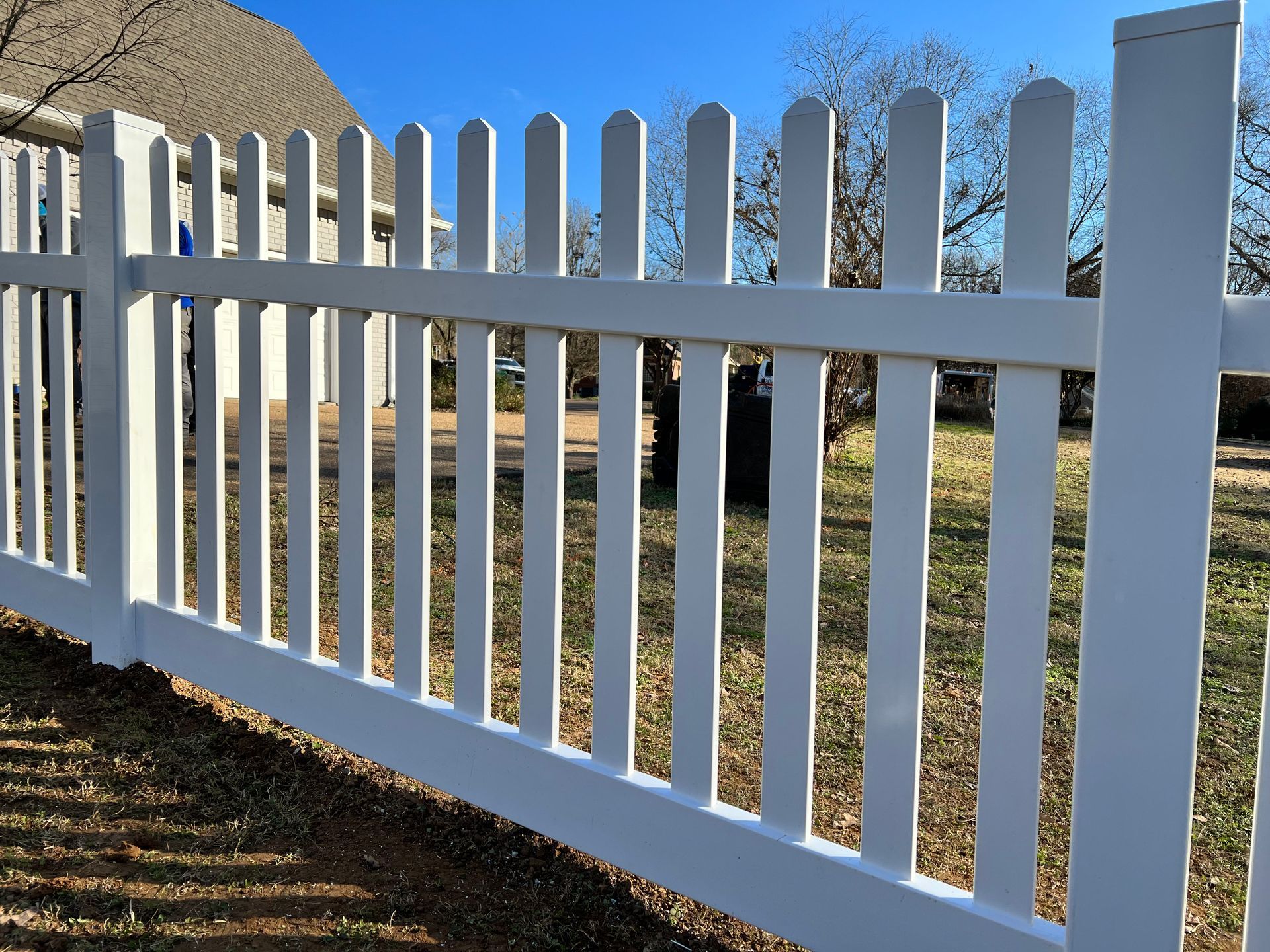 A white picket fence is sitting in the grass in front of a house.