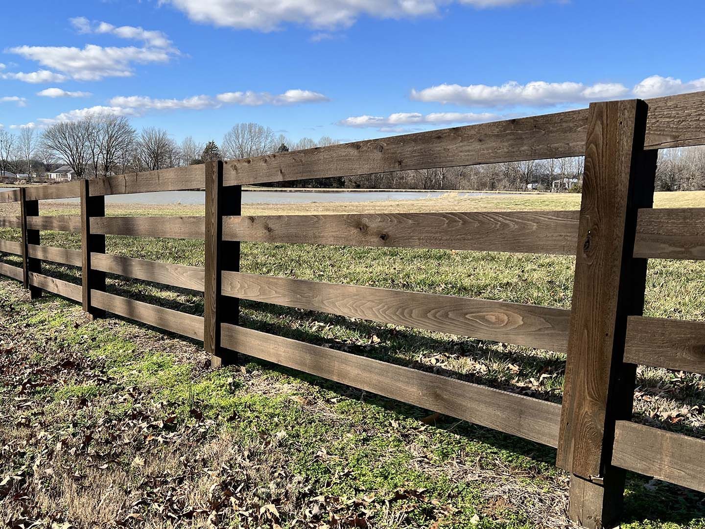 A wooden fence surrounds a grassy field on a sunny day.
