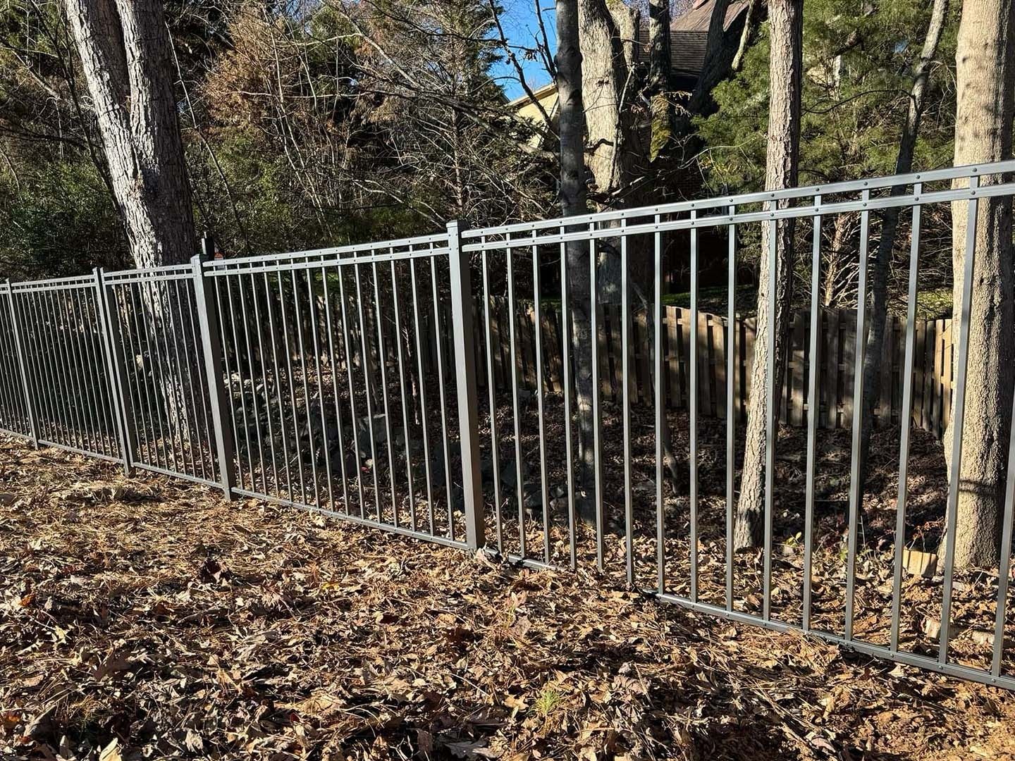 A metal fence is surrounded by trees and leaves in a forest.