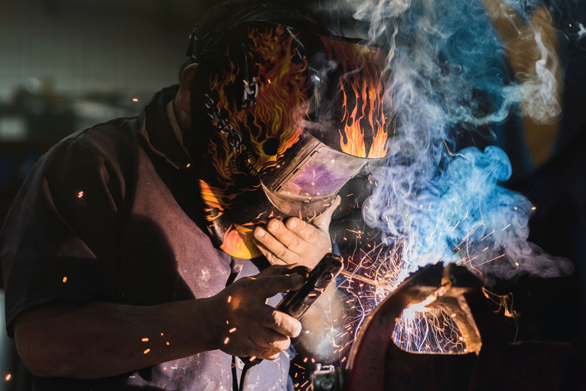 A man wearing a welding mask is welding a piece of metal.