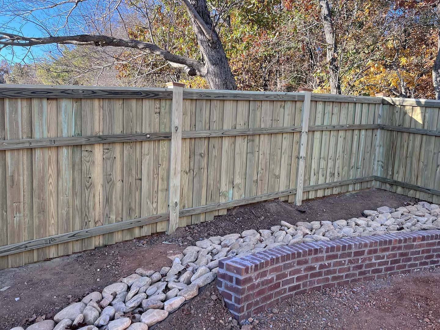 A wooden fence is surrounded by rocks and a brick wall.