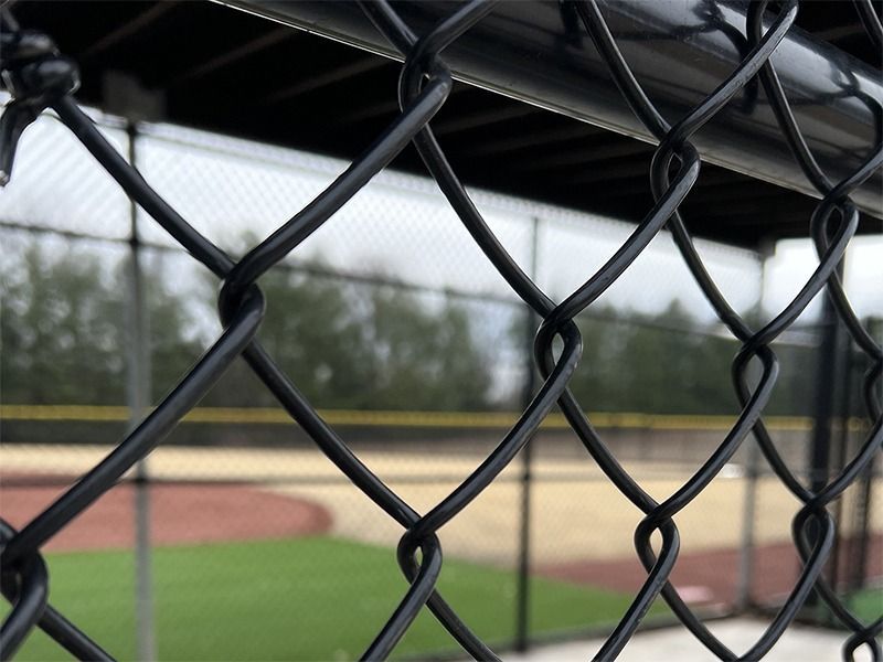 A chain link fence with a baseball field in the background