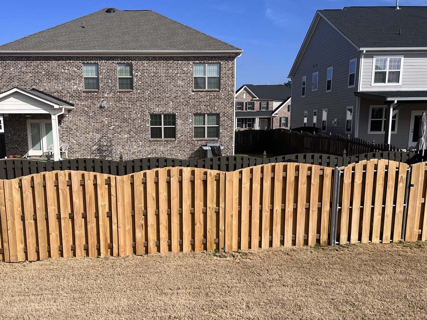 A wooden fence is in front of a brick house.