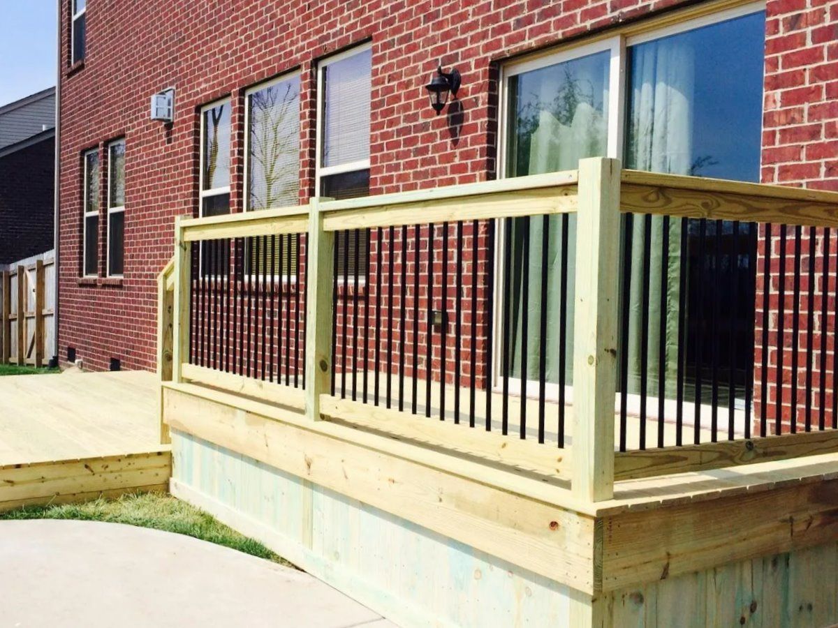 A wooden deck with a black railing is in front of a brick house.