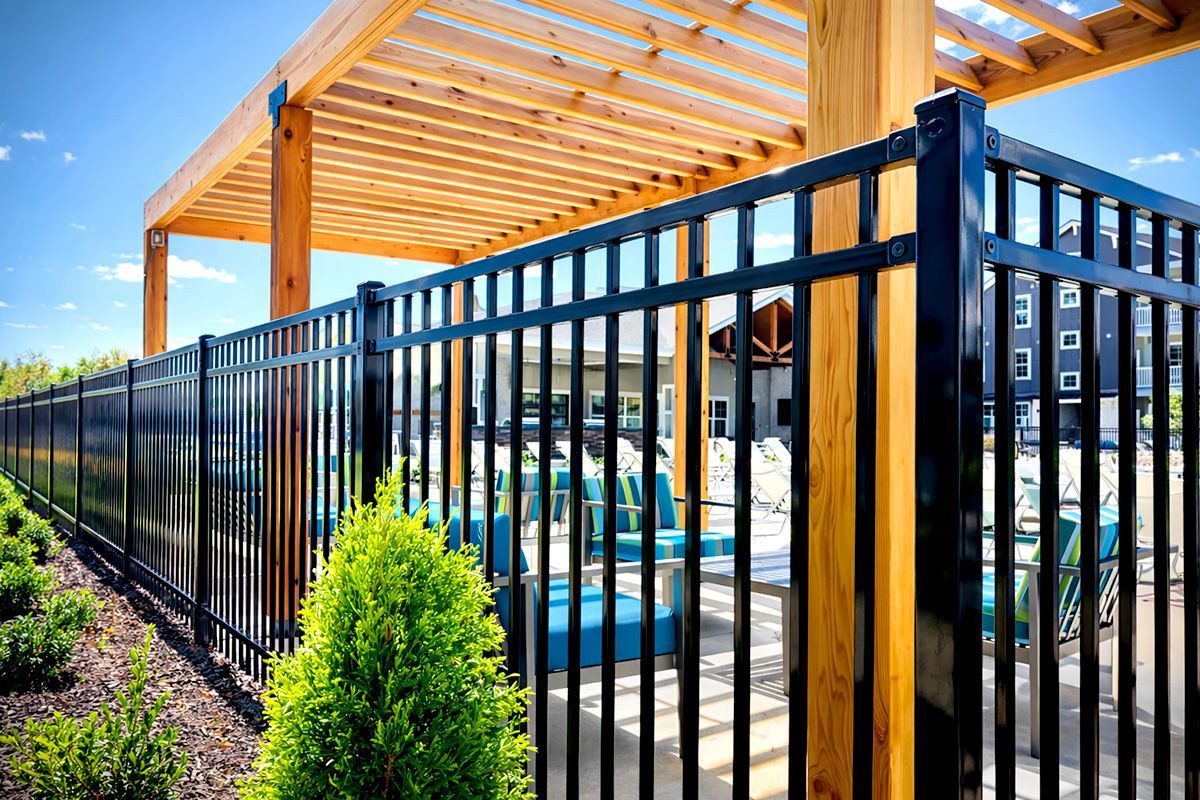 Black metal fence surrounds a pool area with turquoise furniture, under a wooden pergola.