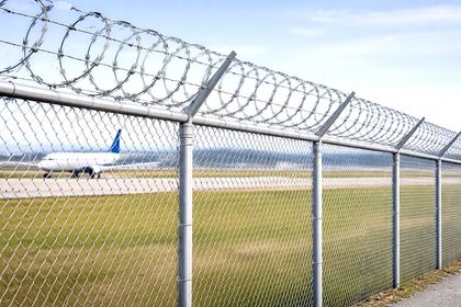 Chain-link fence topped with barbed wire, airfield in background, airplane taxiing on runway.