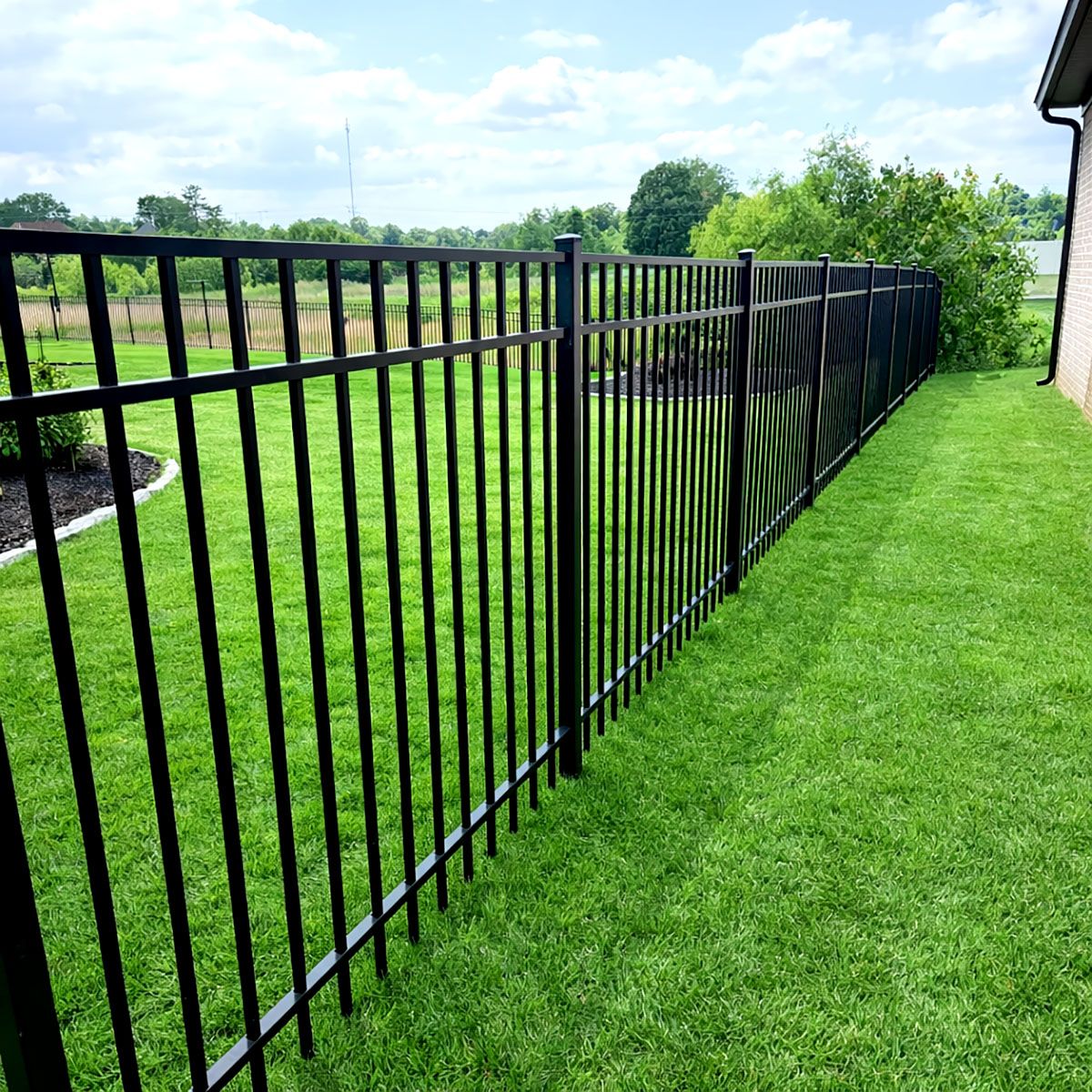 Black metal fence bordering green lawn under a blue sky.