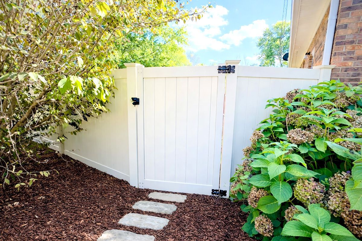 White picket fence with gate, stepping stones, and surrounding foliage.