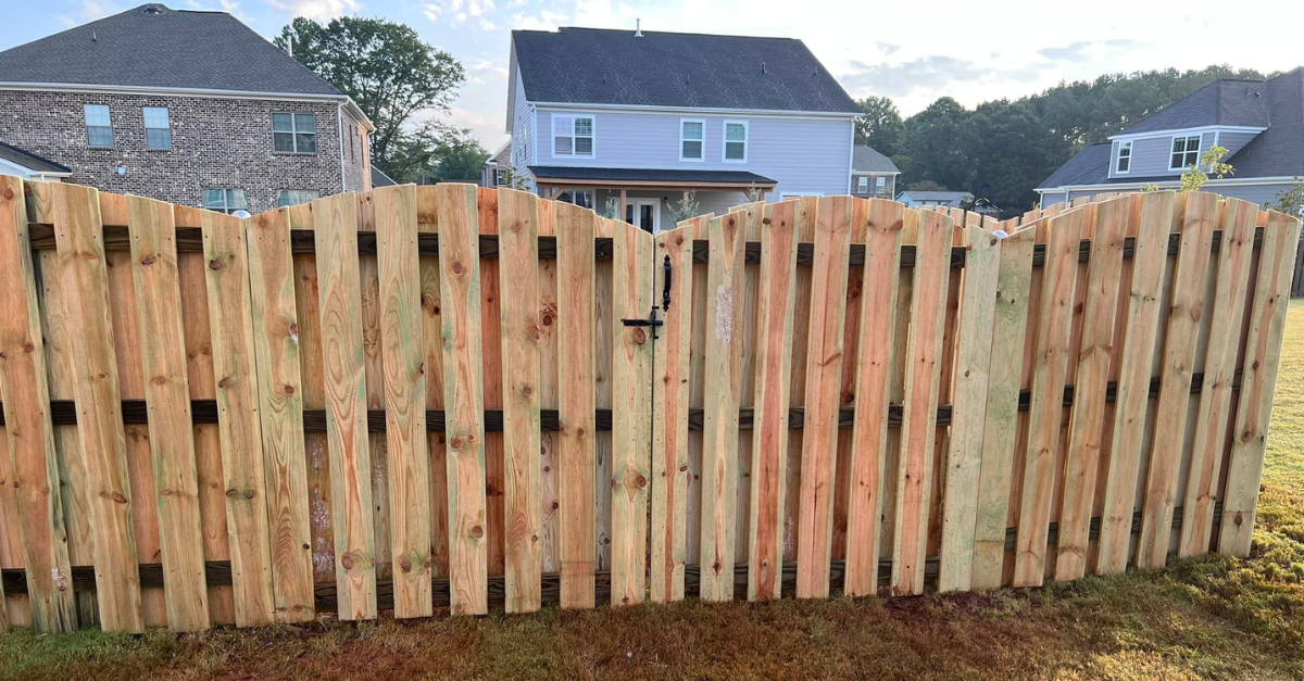Wooden fence with a gate in front of two-story houses.