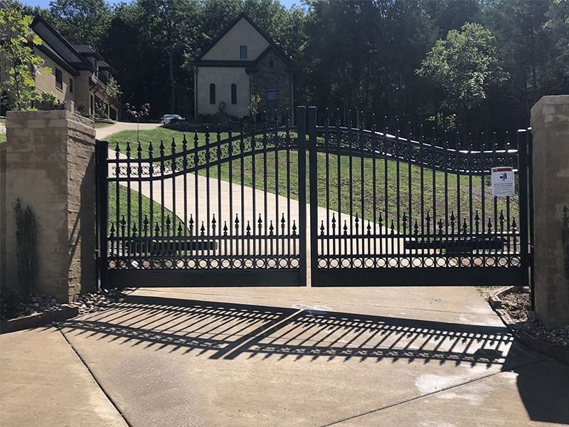 A black gate is open to a driveway in front of a house