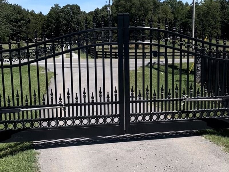 A black wrought iron gate is open to a driveway