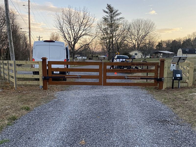 A white van is parked in front of a wooden gate on a gravel road.