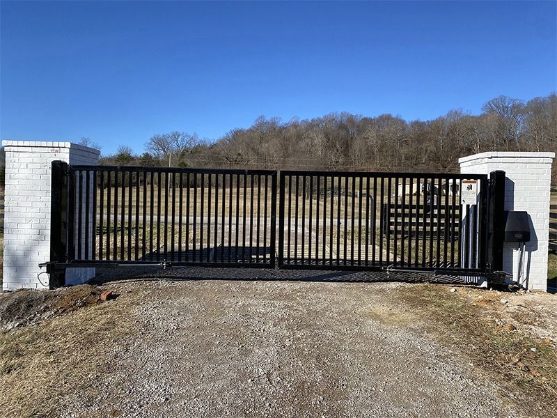 A black gate is sitting on the side of a gravel road.