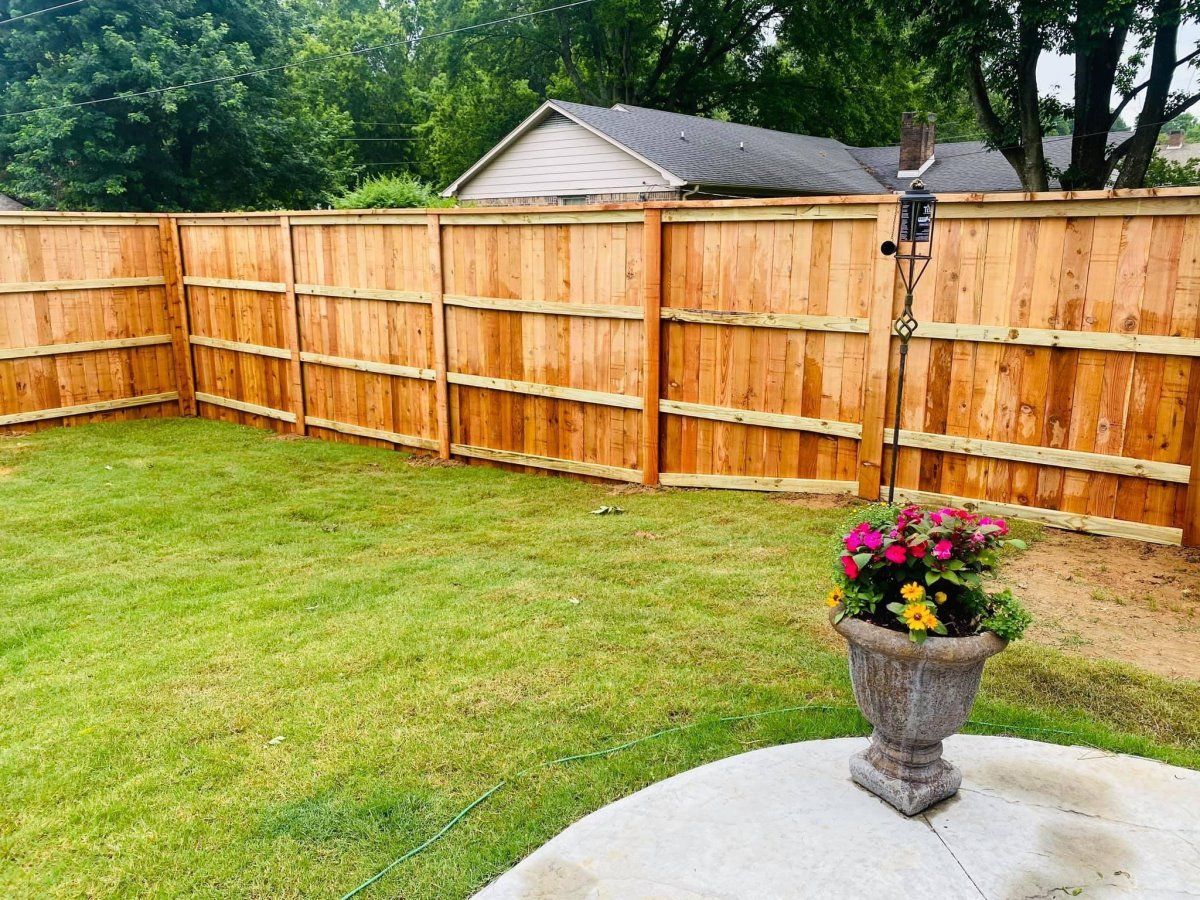 A wooden fence surrounds a lush green lawn in a backyard.