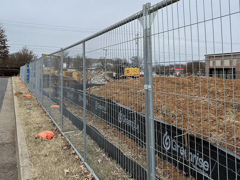 A fence surrounding a construction site with a bulldozer in the background.