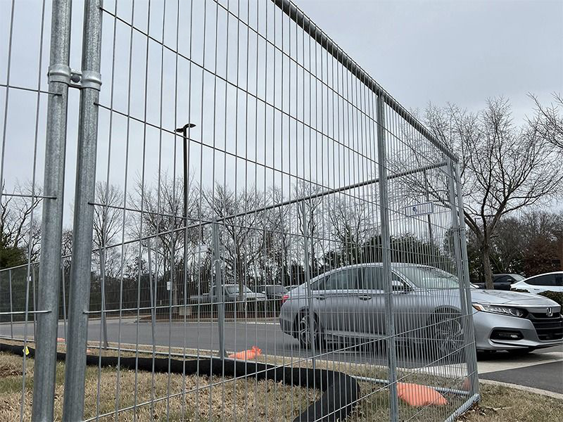 A car is parked behind a fence in a parking lot.