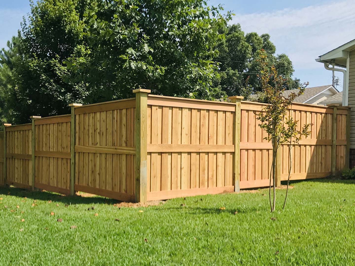 A wooden fence is in the middle of a lush green yard.