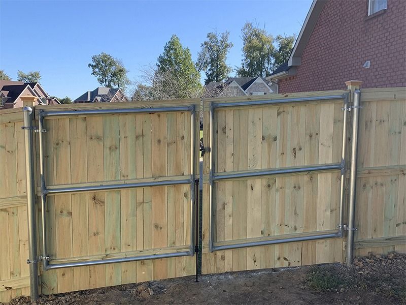 A wooden fence with a metal gate in front of a brick house.