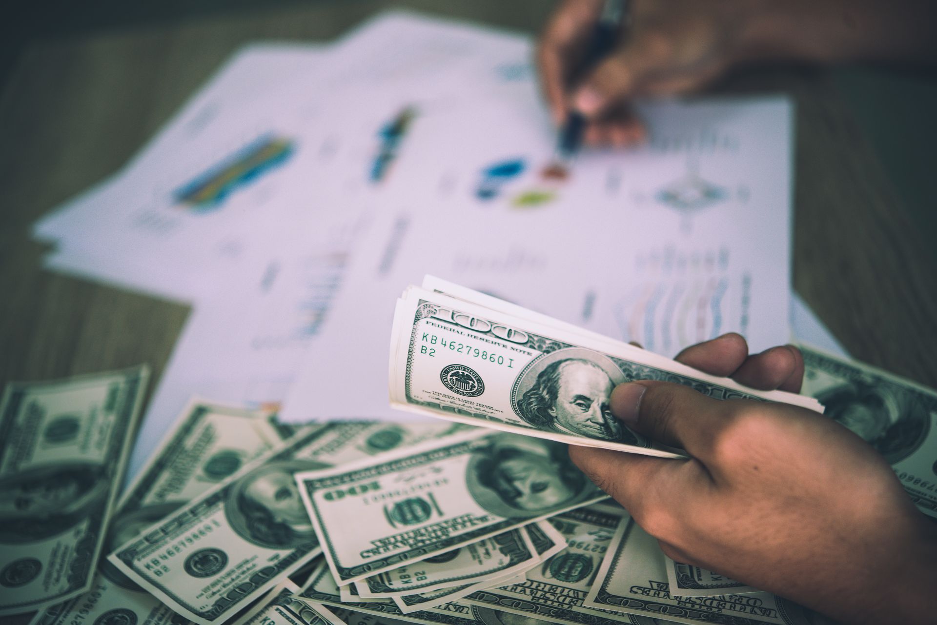 A person is holding a dollar bill in front of a pile of money.