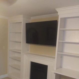 A living room with a fireplace, shelves, and a flat-screen TV.