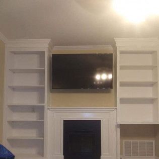 A living room with a fireplace, shelves, and a flat-screen TV.