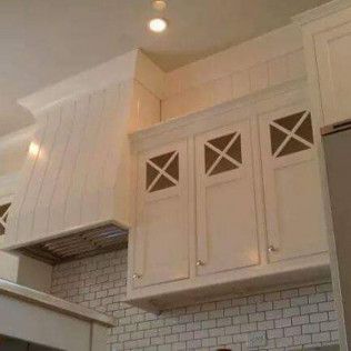 A kitchen with white cabinets and a hood above the cabinets.