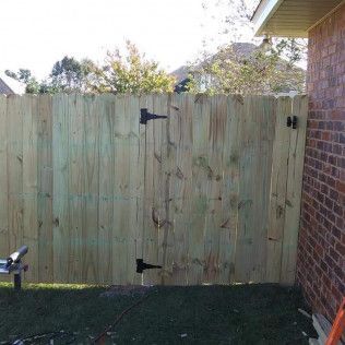 A wooden fence with a gate attached to it is in front of a brick building.