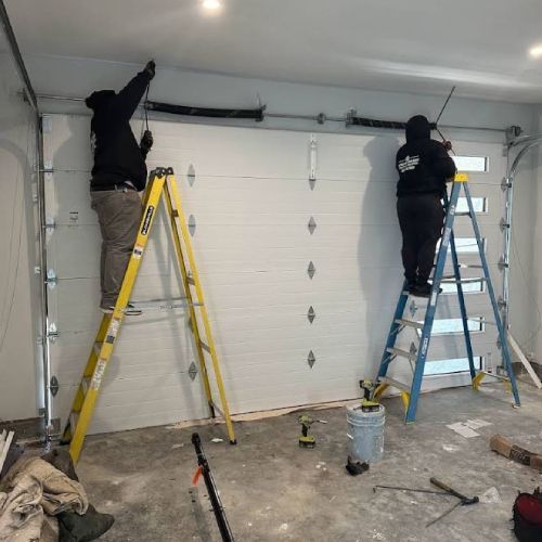 Two men are working on a garage door in a garage.
