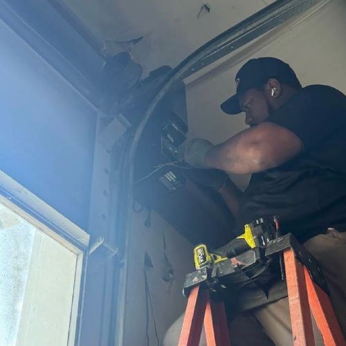 A man is sitting on a ladder working on a garage door.