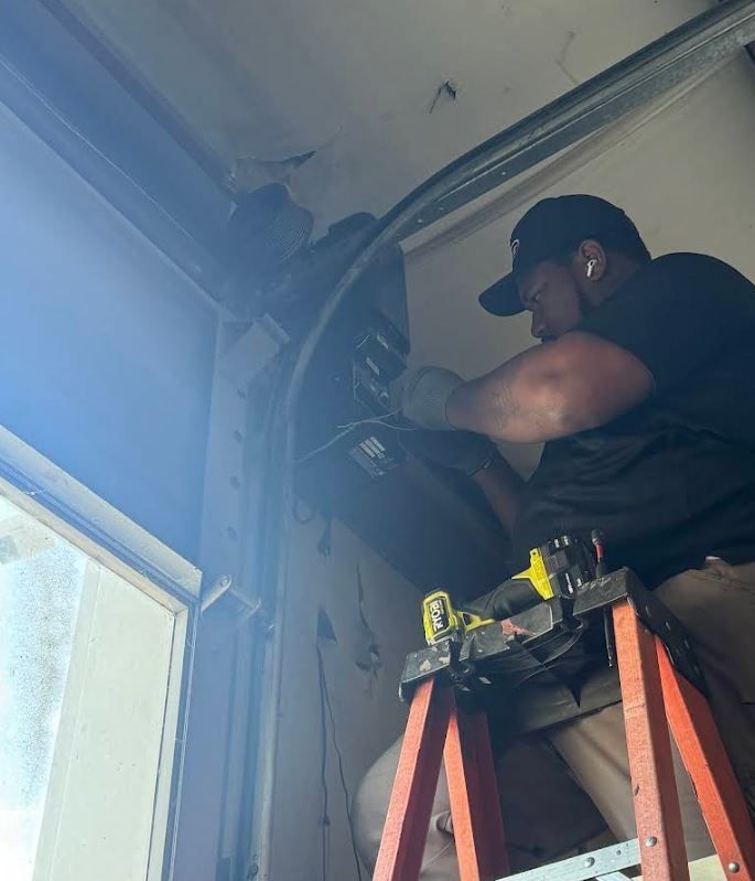 A man is sitting on a ladder working on a garage door.