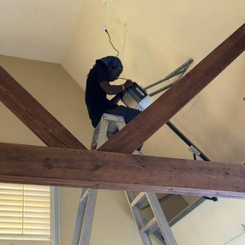 A man is sitting on a ladder working on a garage door