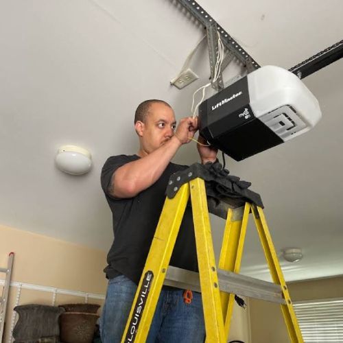 A man is standing on a ladder fixing a garage door opener.