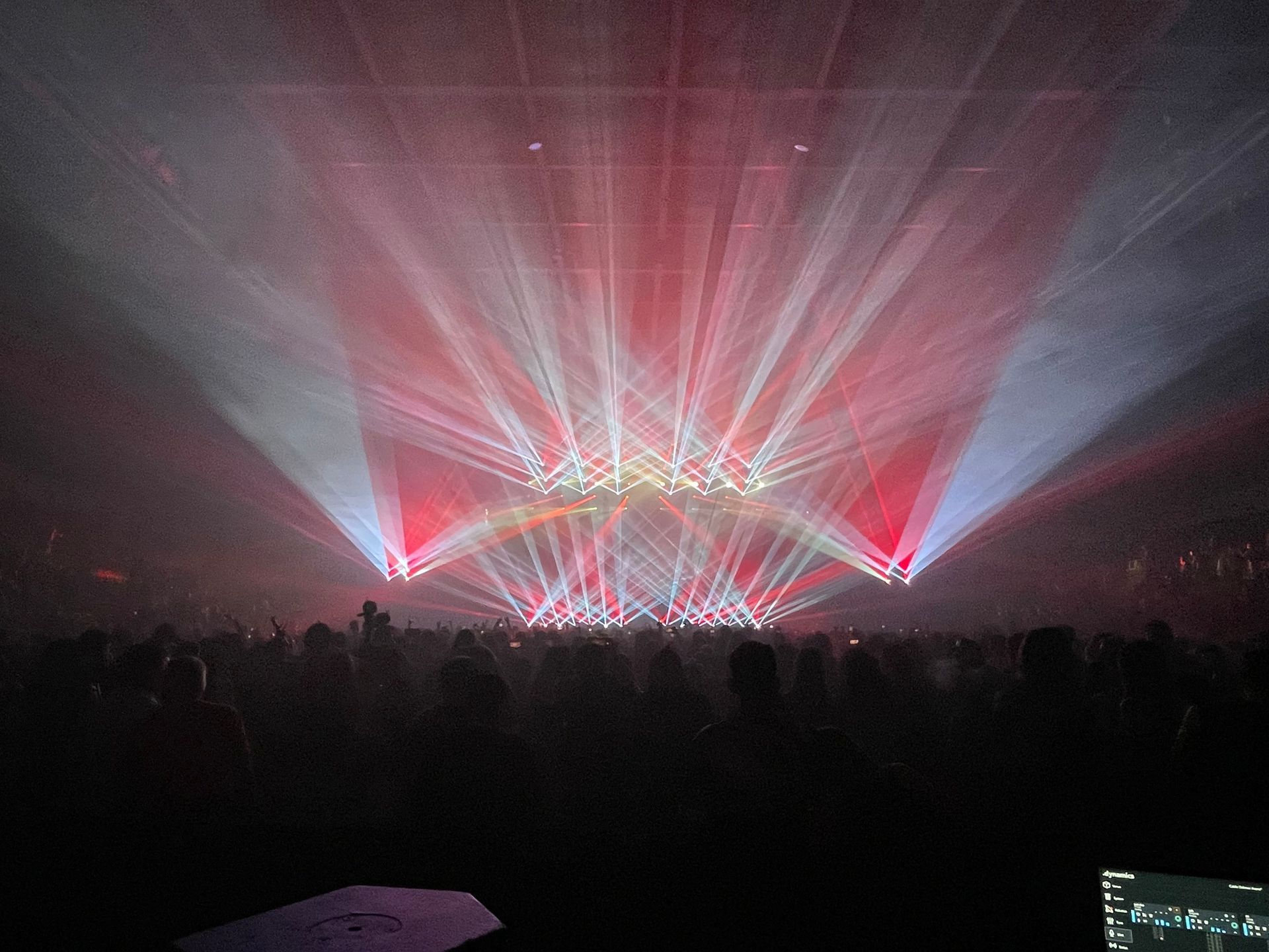 Concert stage with red and white lights beaming over a dark crowd.