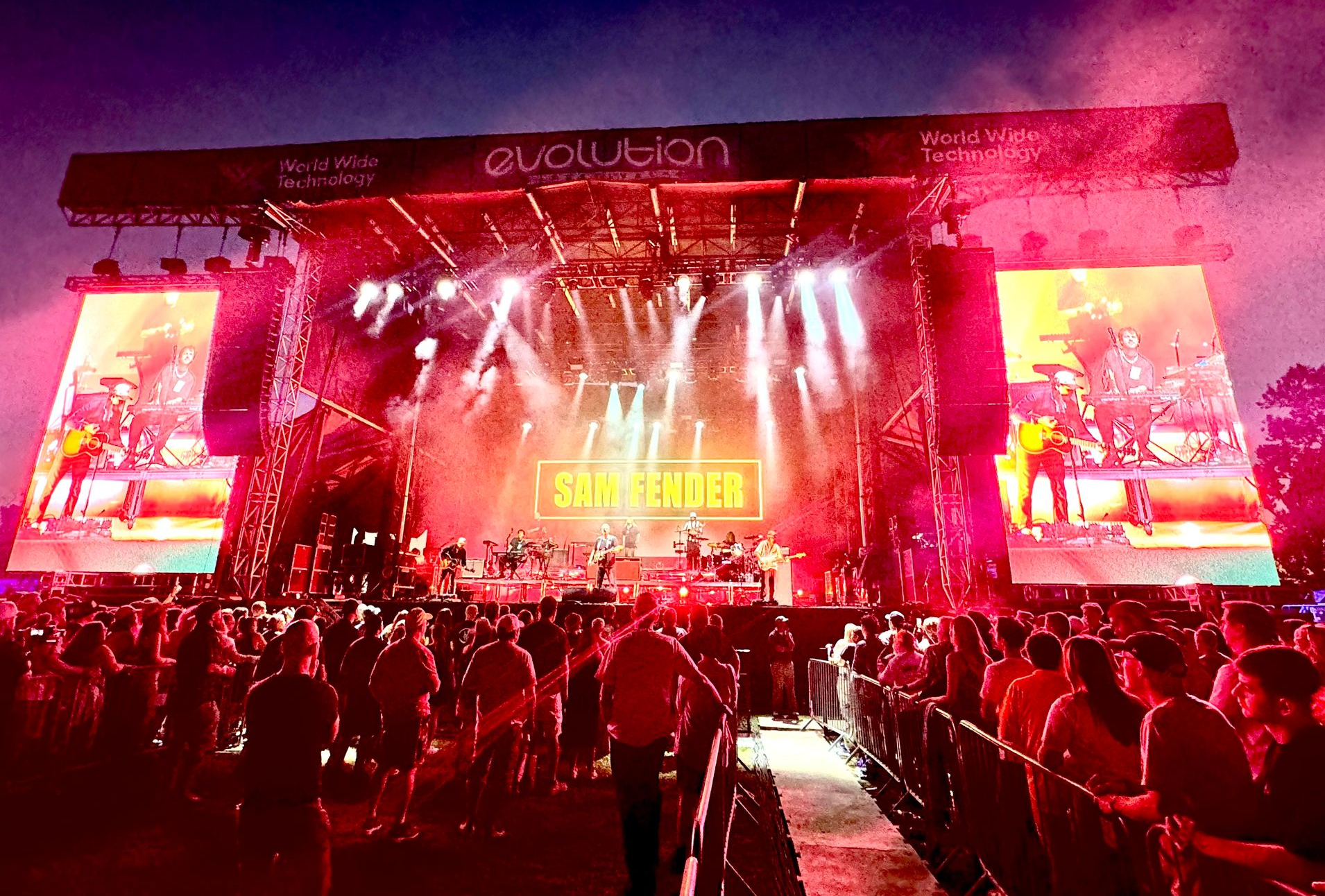 Concert stage with a band silhouetted against blue and white lights and a laser beam.