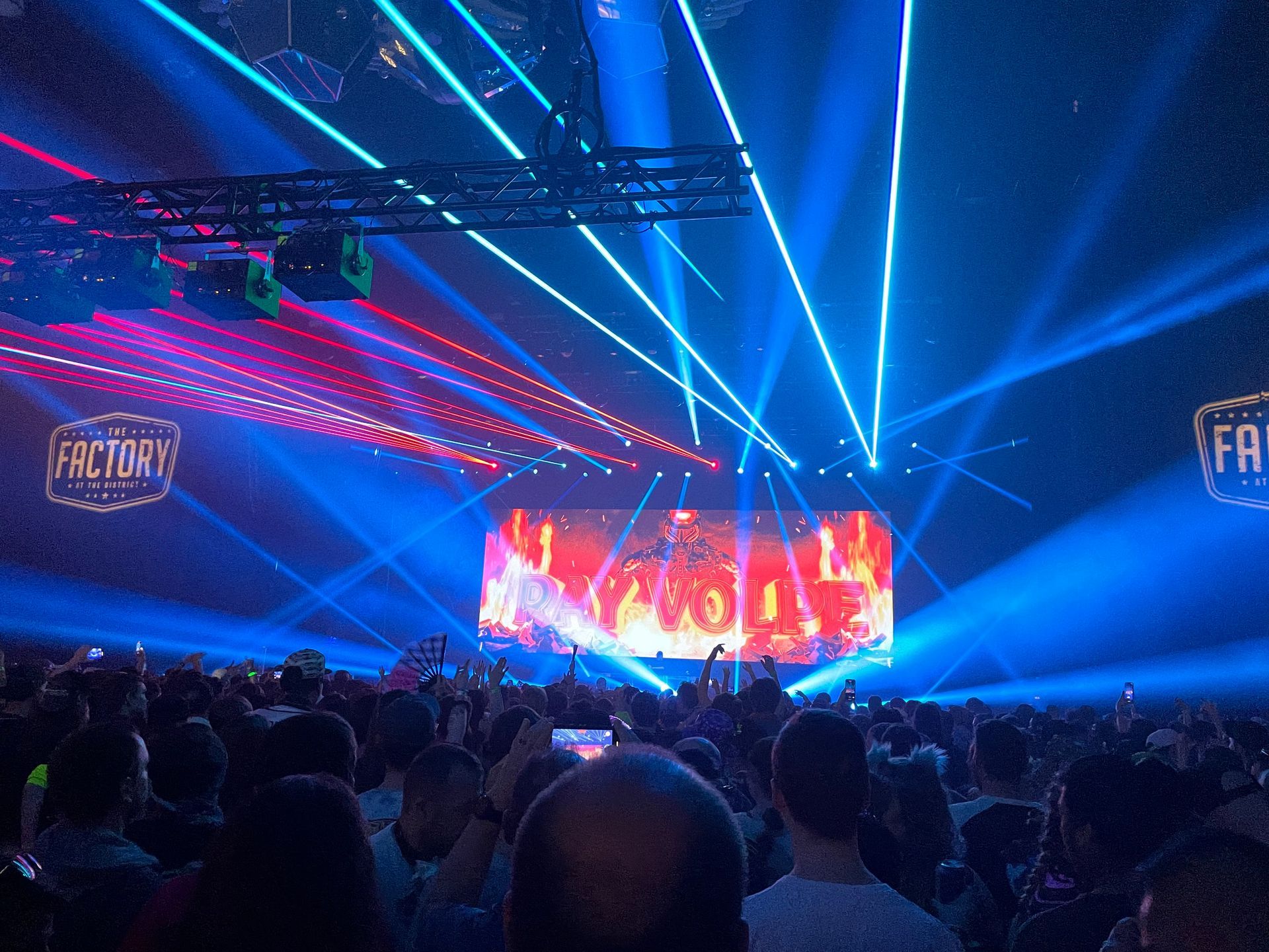 Concert crowd with blue and red stage lights, spotlights, and screen displaying performers at Factory event.