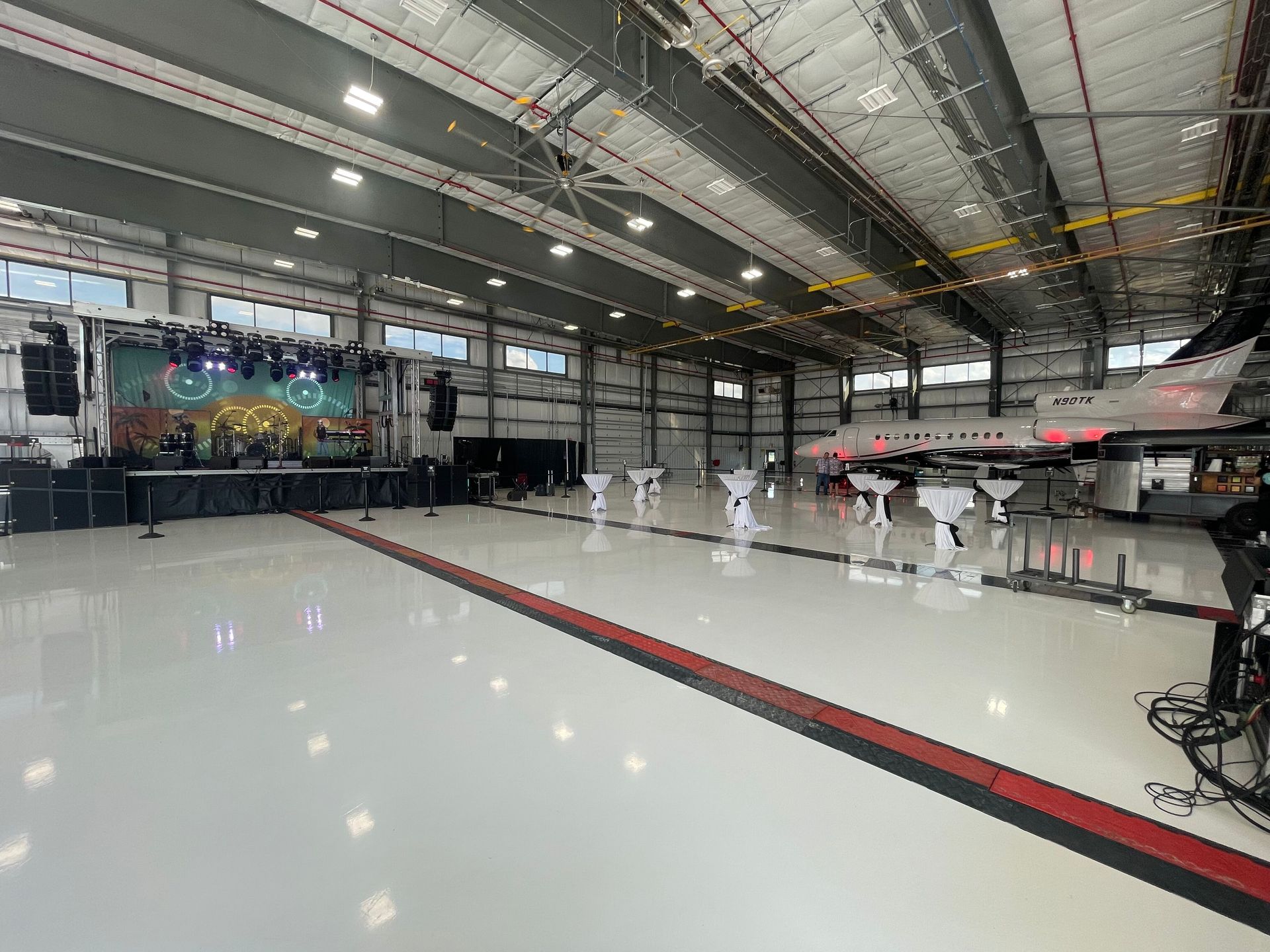 An event in an airplane hangar with a stage, tables, and an airplane. Shiny floor.