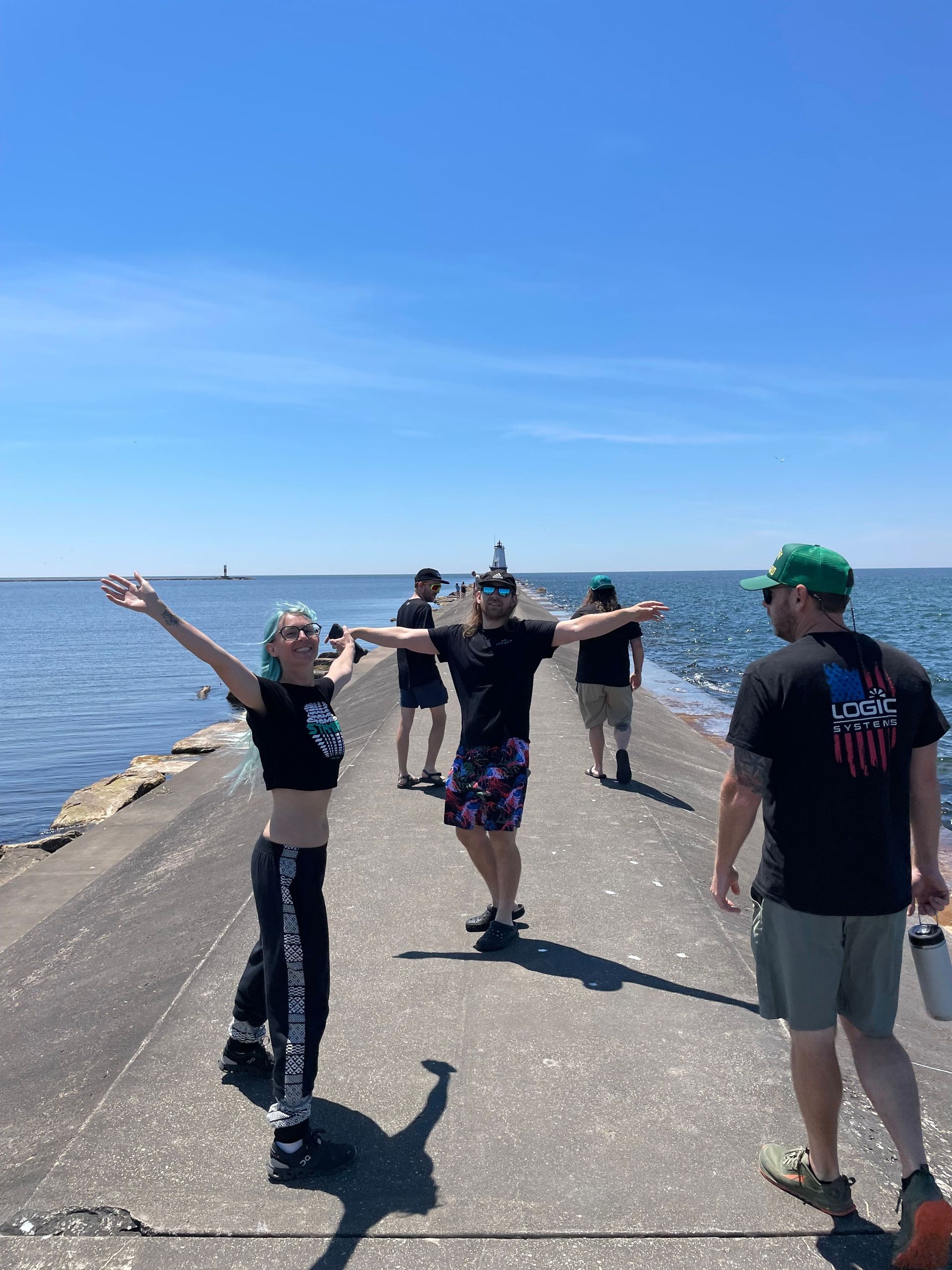 People with arms outstretched on a concrete pier by the sea on a sunny day.