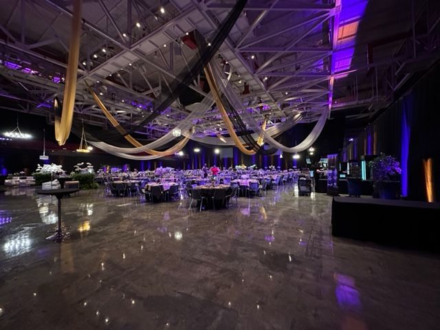 Large event space set for a gathering, tables arranged. Purple lighting accents metallic ceiling and draping fabric.