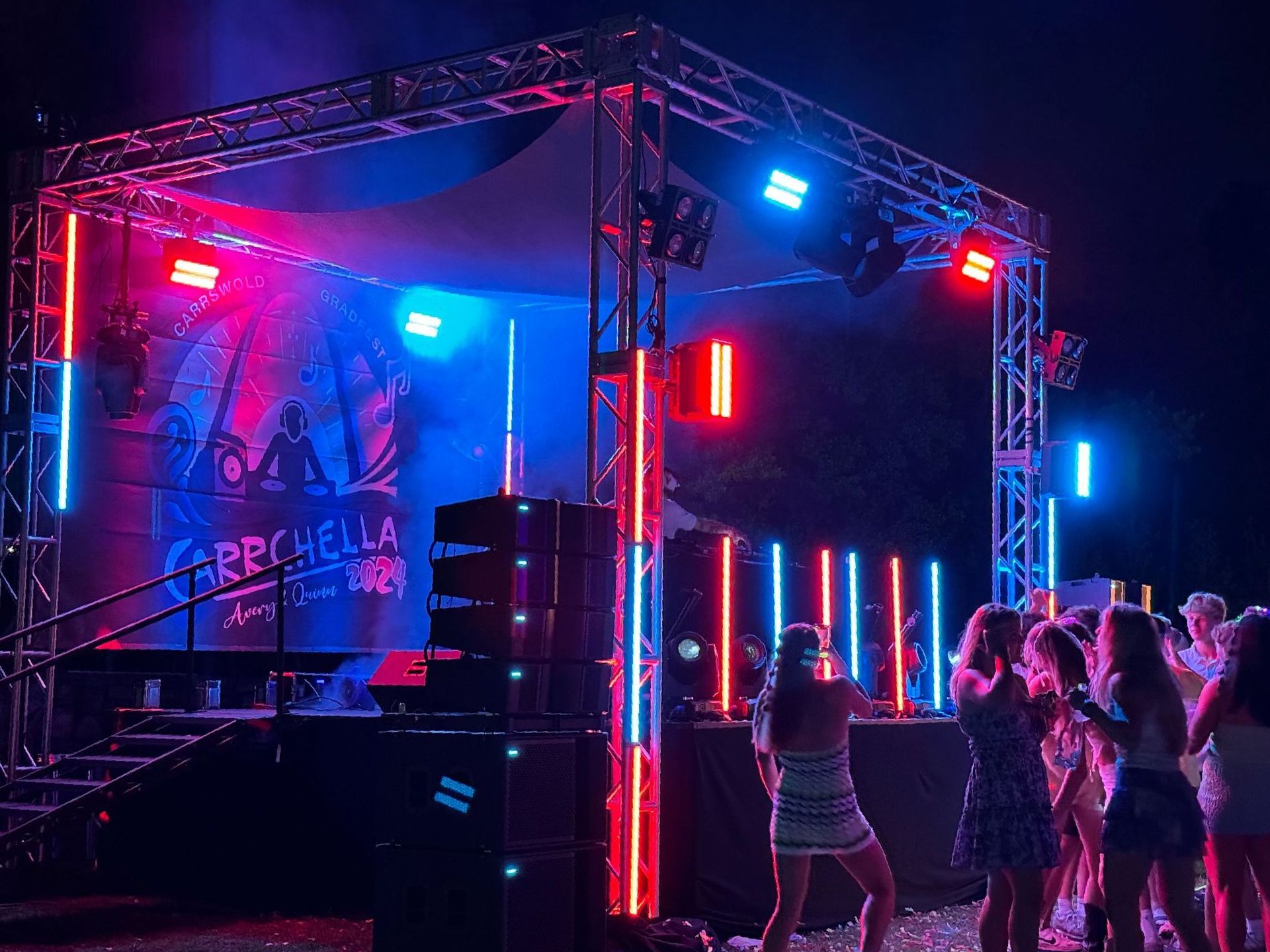 Stage at night with colorful lights and people dancing. A banner reads 